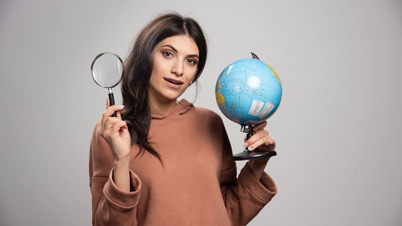 زن جوان با ذره‌بین و کره زمین در دست
